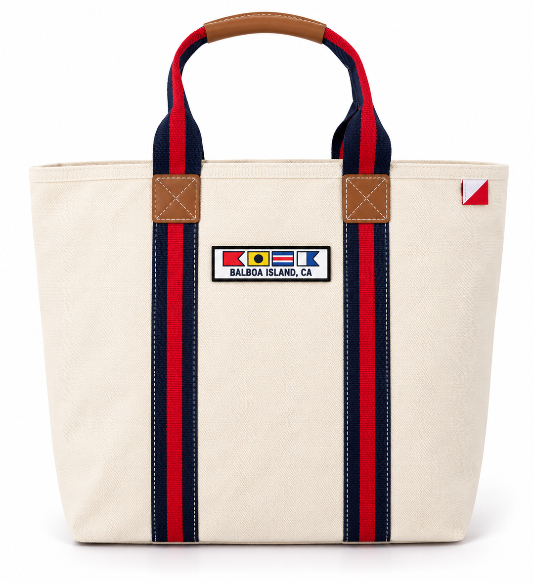 An off-white canvas tote bag with red and navy striped handles, brown leather accents, and a 'Balboa Island, CA' flag patch on the front.