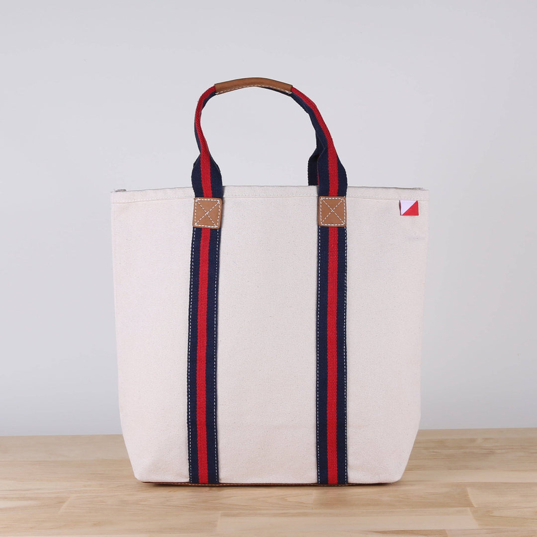 White tote bag with red and blue straps on a wooden surface