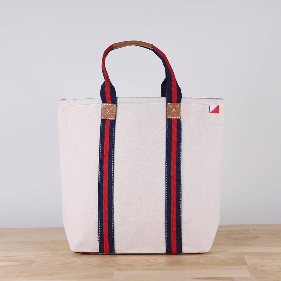 White tote bag with red and blue straps on a wooden surface