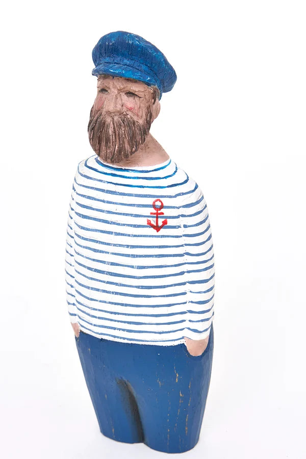 A painted wooden sailor figurine with a blue cap, blue pants, a blue and white striped shirt with a small red anchor emblem, and a brown beard, shown against a plain white background.