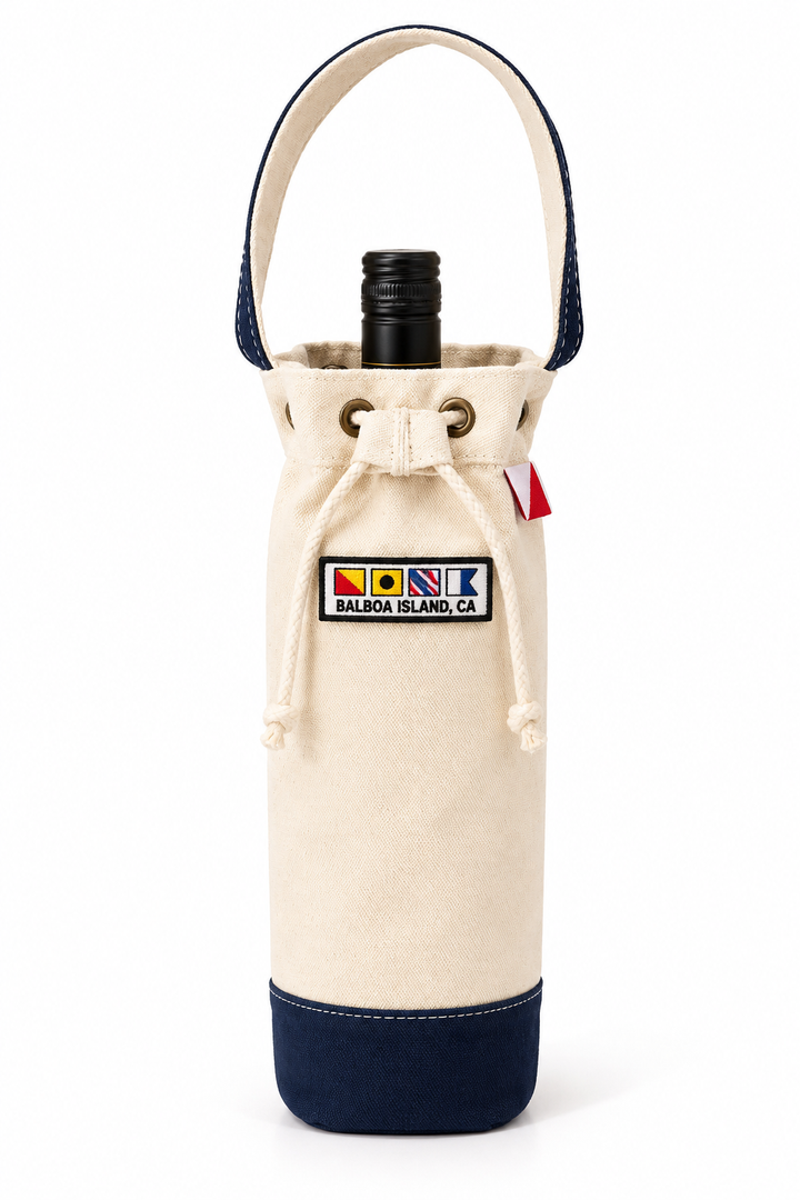 An off-white canvas wine bottle carrier with navy blue trim, a top handle, and a drawstring closure, featuring a 'NISK Balboa Island, CA' patch on the front.
