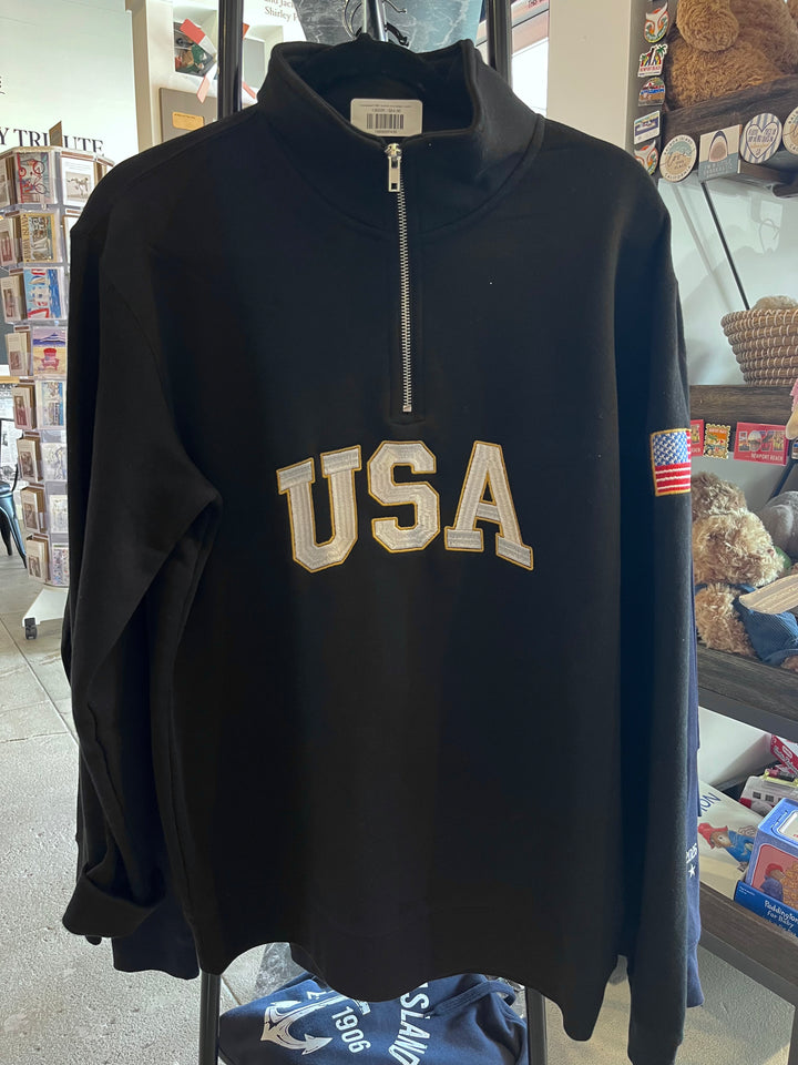 A black long-sleeve quarter-zip sweatshirt with 'USA' embroidered in gold and white across the chest, featuring a small American flag patch on the right sleeve, displayed on a hanger in a retail store.