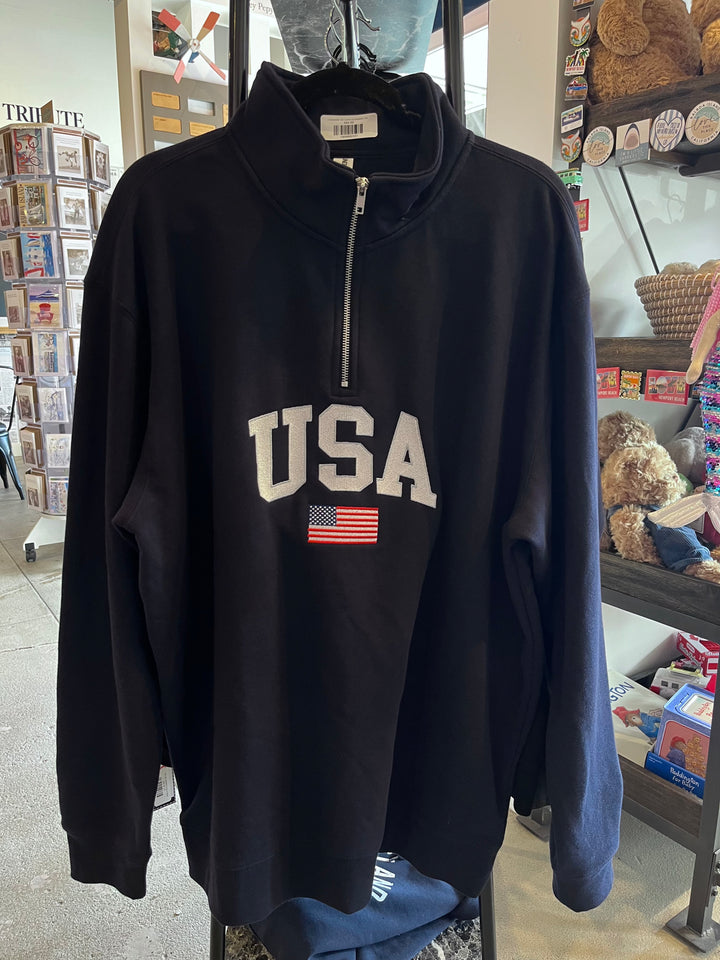 A black long-sleeve quarter-zip sweatshirt with 'USA' and an American flag graphic on the front, hanging in a retail store.