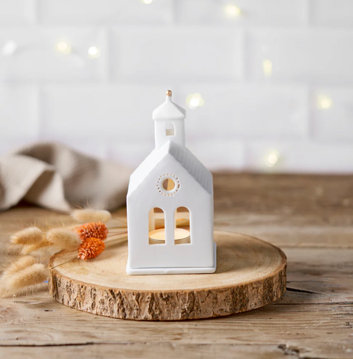 White ceramic church-shaped lantern on a wooden surface with a soft, blurred background