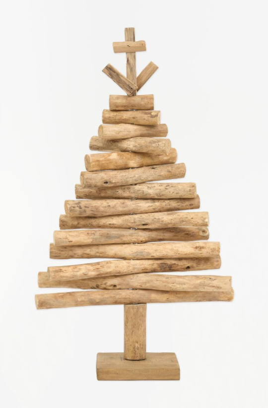 A rustic, handcrafted Christmas tree made from stacked natural driftwood logs of varying sizes, standing on a square wooden base with a matching cross-shaped topper, set against a plain white background.