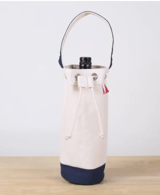 A canvas wine bottle carrier bag in off-white and navy blue, shown holding a stainless steel wine bottle on a light wood surface against a plain white background.