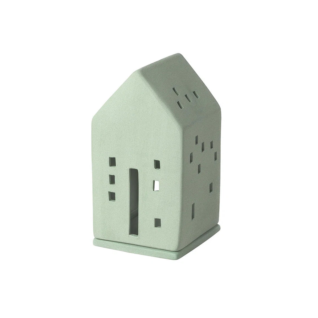 A small house-shaped ceramic candle holder or lantern in a pale sage green color, featuring cutout windows and a door, shown on a plain white background.