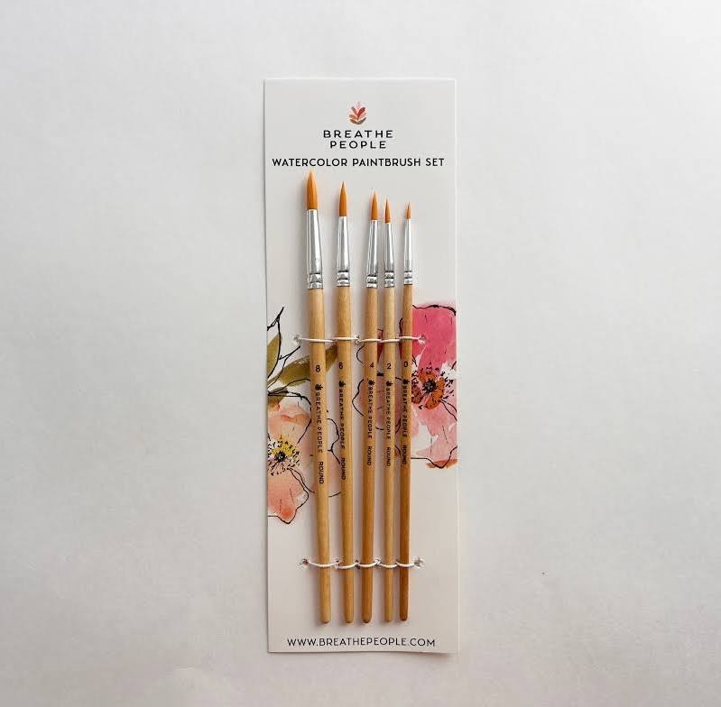 A watercolor paintbrush set by Breathe People, featuring five wooden-handled brushes with orange bristles, presented on a white backing card with floral illustrations.